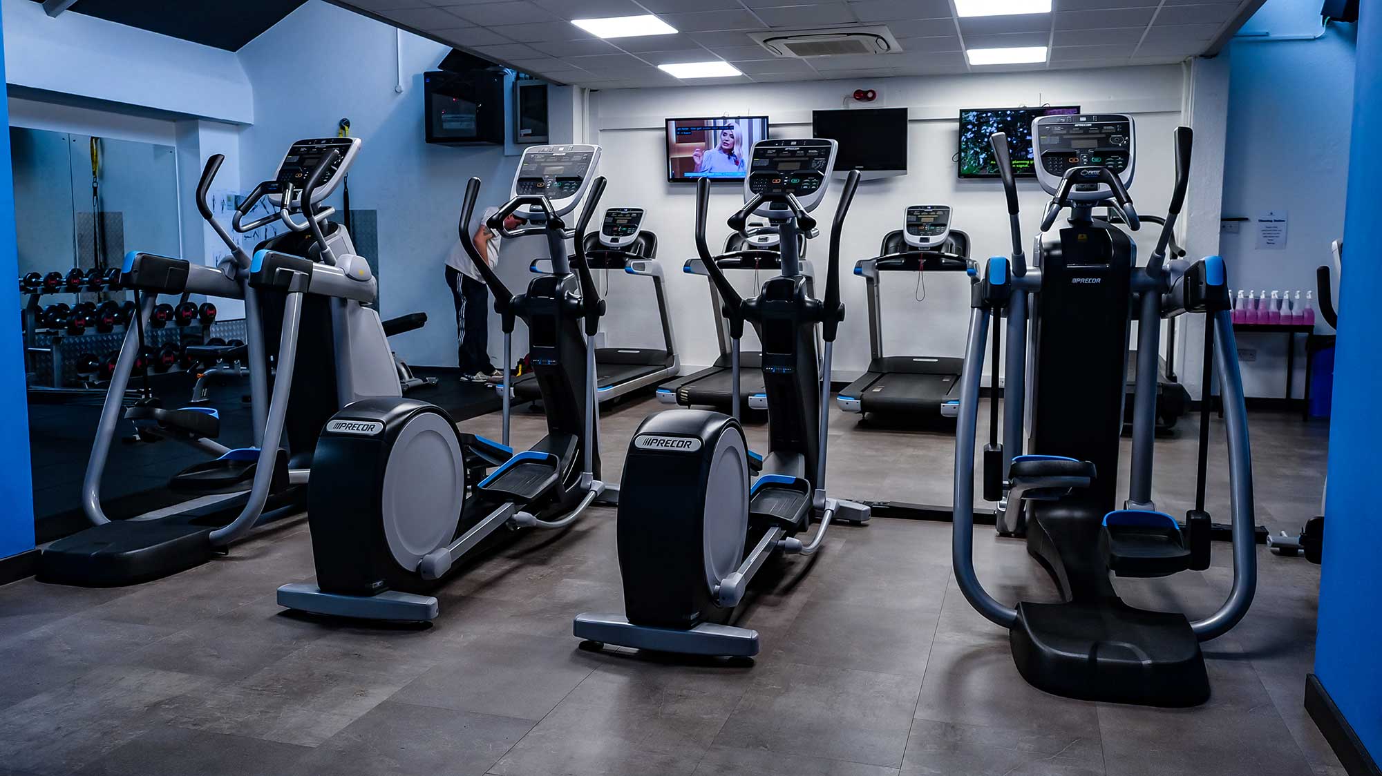 Picture showing two rows of gym equipment, with stepping machines in the foreground and treadmillls in the background